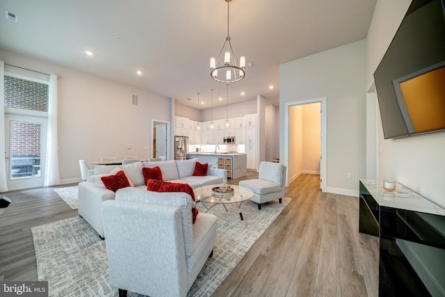 living area featuring light wood finished floors, recessed lighting, visible vents, an inviting chandelier, and baseboards