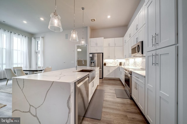 kitchen with tasteful backsplash, a center island with sink, appliances with stainless steel finishes, wood finished floors, and a sink