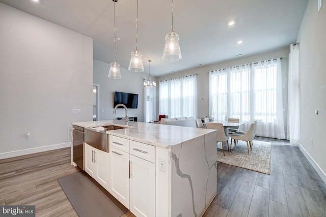 kitchen with light wood finished floors, white cabinets, a kitchen island with sink, a sink, and dishwasher