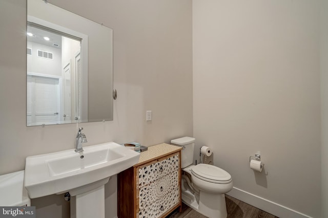 half bath with toilet, wood finished floors, a sink, visible vents, and baseboards