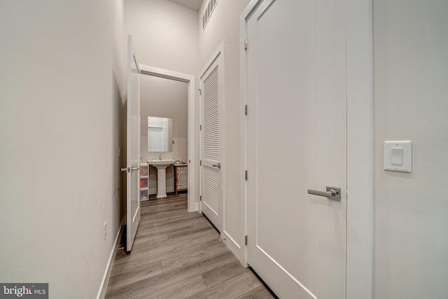 corridor featuring light wood-style floors, visible vents, and a sink