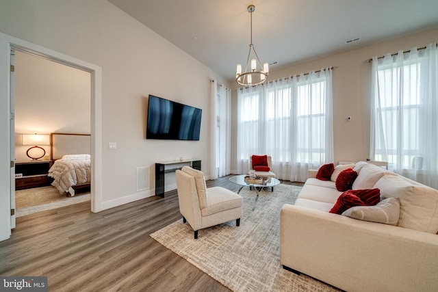 living area featuring a chandelier, wood finished floors, visible vents, and baseboards