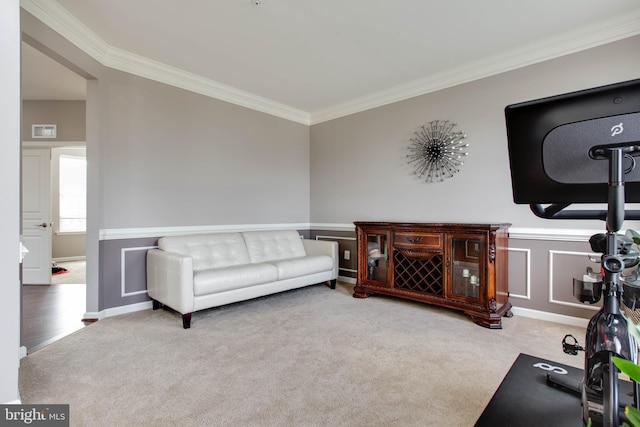 carpeted living area with a wainscoted wall, ornamental molding, visible vents, and a decorative wall