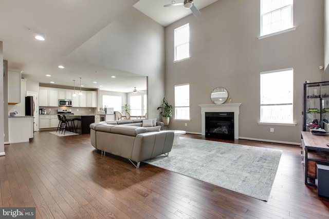 living area with dark wood-style floors, baseboards, a ceiling fan, and a glass covered fireplace