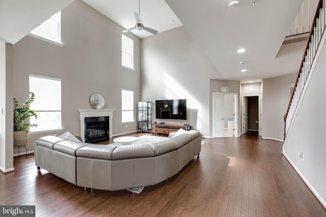 living room featuring stairway, dark wood finished floors, a wealth of natural light, and a glass covered fireplace