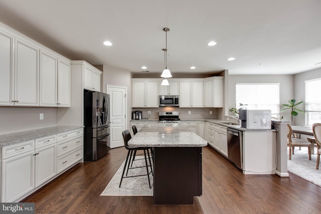 kitchen featuring appliances with stainless steel finishes, dark wood-style flooring, a kitchen bar, and white cabinetry