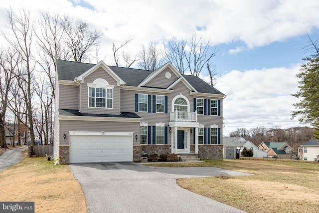 view of front of property with an attached garage, a balcony, stone siding, driveway, and a front yard