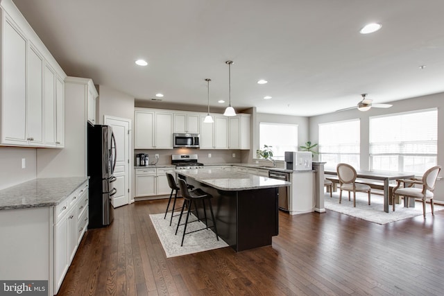 kitchen with white cabinets, dark wood finished floors, a kitchen island, stainless steel appliances, and recessed lighting