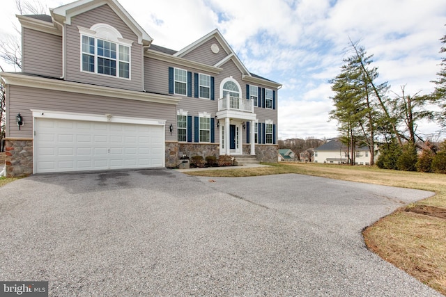 view of front of house featuring aphalt driveway, stone siding, a balcony, and an attached garage