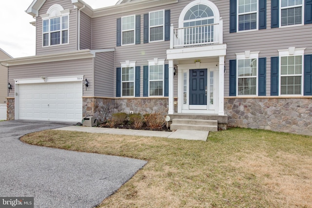 view of front of property featuring a front lawn, stone siding, driveway, and an attached garage