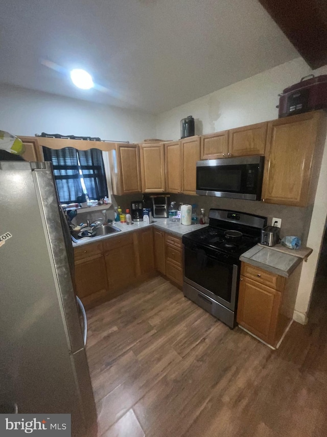 kitchen featuring light countertops, stainless steel appliances, a sink, and wood finished floors