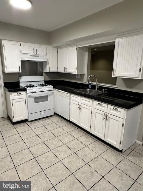 kitchen with white appliances, dark countertops, under cabinet range hood, white cabinetry, and a sink