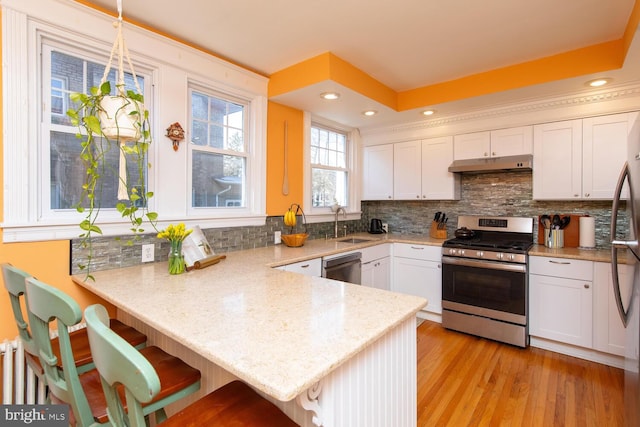 kitchen featuring under cabinet range hood, appliances with stainless steel finishes, a peninsula, and white cabinetry