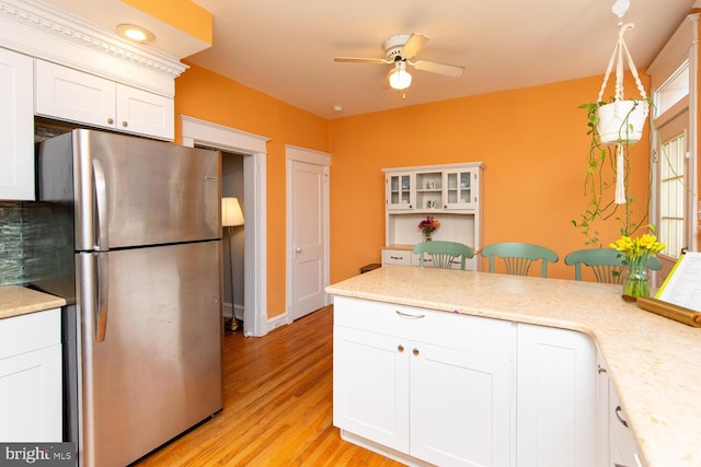 kitchen with a peninsula, freestanding refrigerator, ceiling fan, white cabinets, and light wood-type flooring