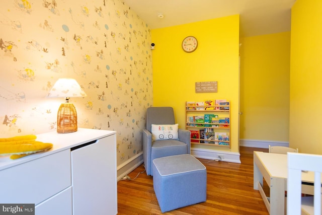 living area with baseboards, wood finished floors, and wallpapered walls