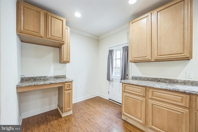 kitchen with baseboards, light wood-type flooring, built in study area, light brown cabinetry, and crown molding