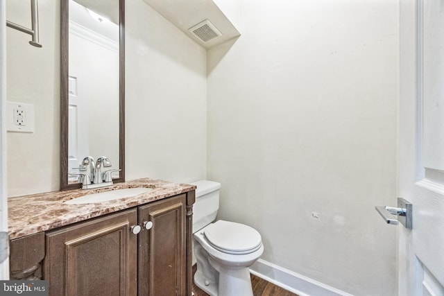 half bathroom with visible vents, toilet, vanity, wood finished floors, and baseboards