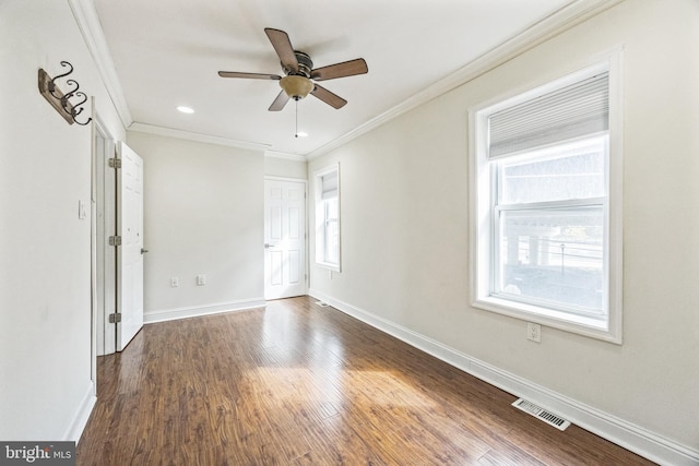 empty room with a healthy amount of sunlight, visible vents, dark wood-type flooring, and ornamental molding