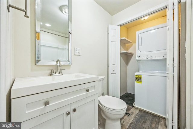 half bathroom with toilet, vanity, stacked washer / dryer, and wood finished floors