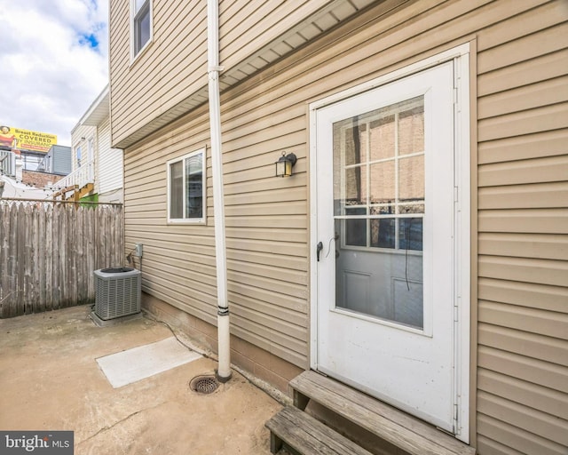 view of exterior entry featuring a patio, cooling unit, and fence