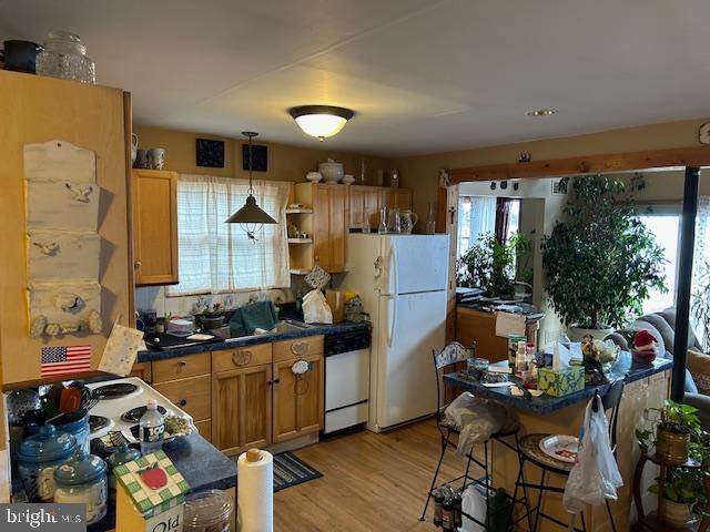 kitchen with open shelves, dark countertops, hanging light fixtures, light wood-style flooring, and white appliances