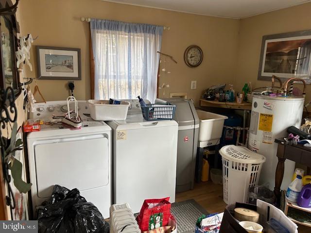 laundry room featuring water heater, washing machine and dryer, a sink, wood finished floors, and laundry area