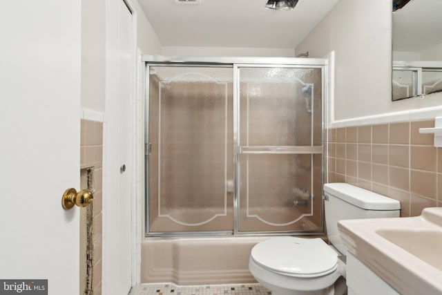 full bath featuring toilet, combined bath / shower with glass door, wainscoting, and tile walls