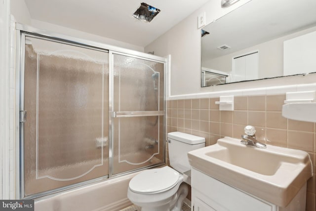 bathroom featuring tile walls, bath / shower combo with glass door, visible vents, toilet, and vanity