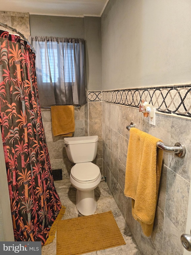 full bath with a shower with shower curtain, wainscoting, tile walls, and toilet