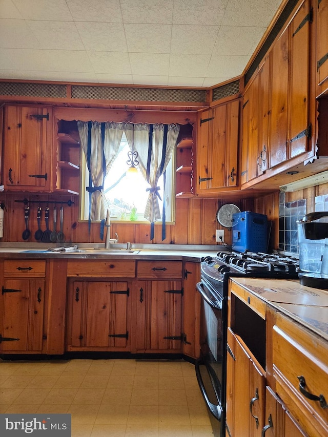 kitchen with a sink, light countertops, brown cabinets, open shelves, and black gas range oven