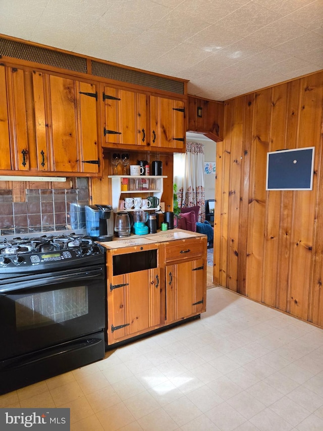 kitchen with wood walls, brown cabinetry, and black gas range