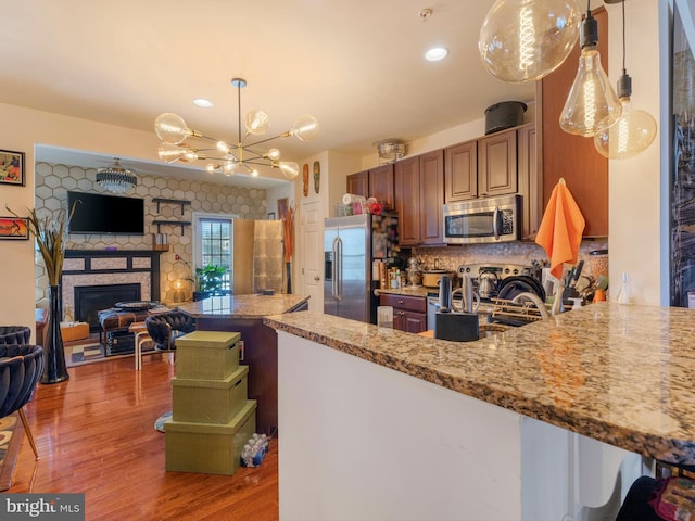 kitchen with tasteful backsplash, wood finished floors, a stone fireplace, appliances with stainless steel finishes, and light stone countertops