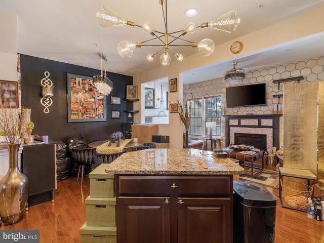 kitchen featuring light stone counters, wood finished floors, open floor plan, a fireplace, and a chandelier