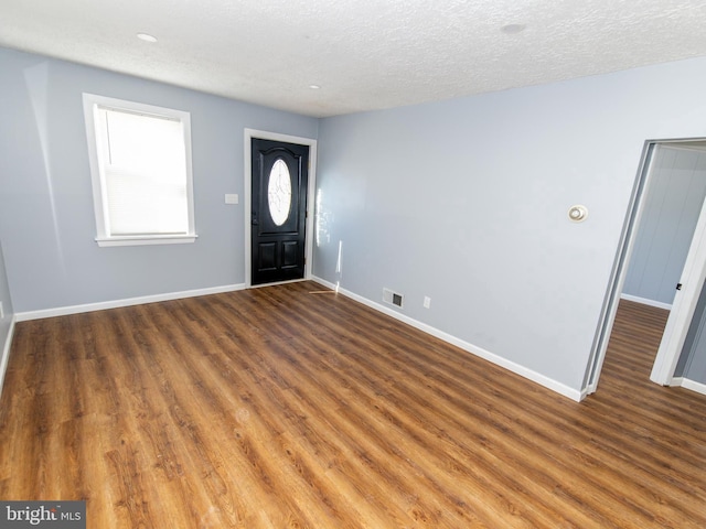 entryway with a textured ceiling, wood finished floors, visible vents, and baseboards