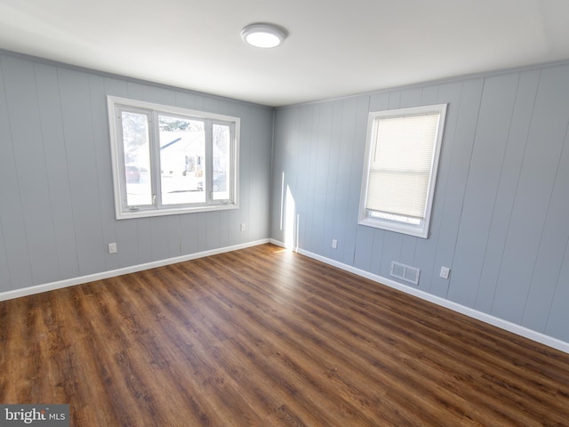 empty room with dark wood-style floors, baseboards, and visible vents