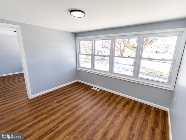 empty room featuring dark wood-type flooring, visible vents, and baseboards