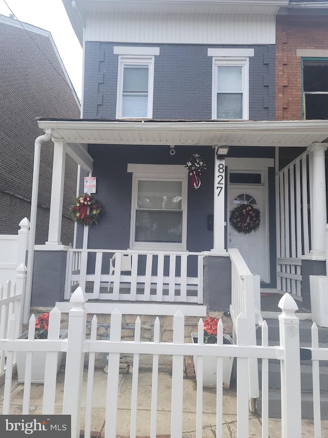 entrance to property featuring a porch, fence, and brick siding