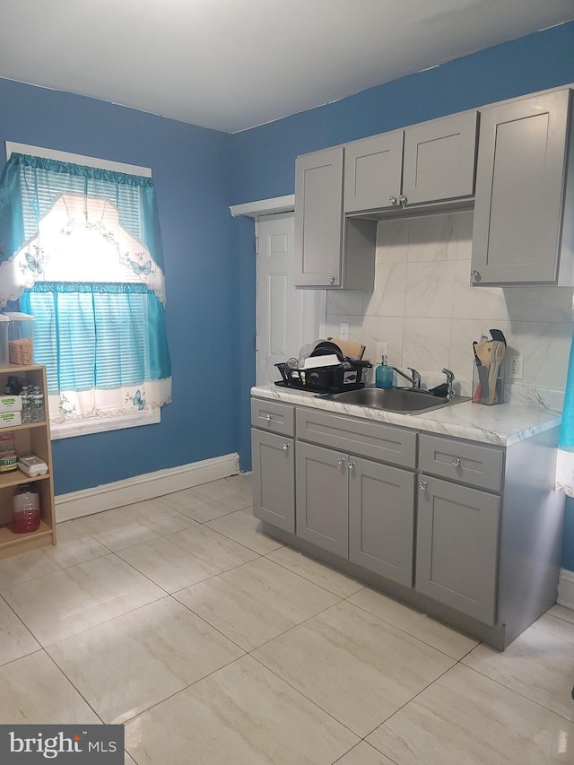 kitchen with baseboards, a sink, light countertops, gray cabinetry, and backsplash