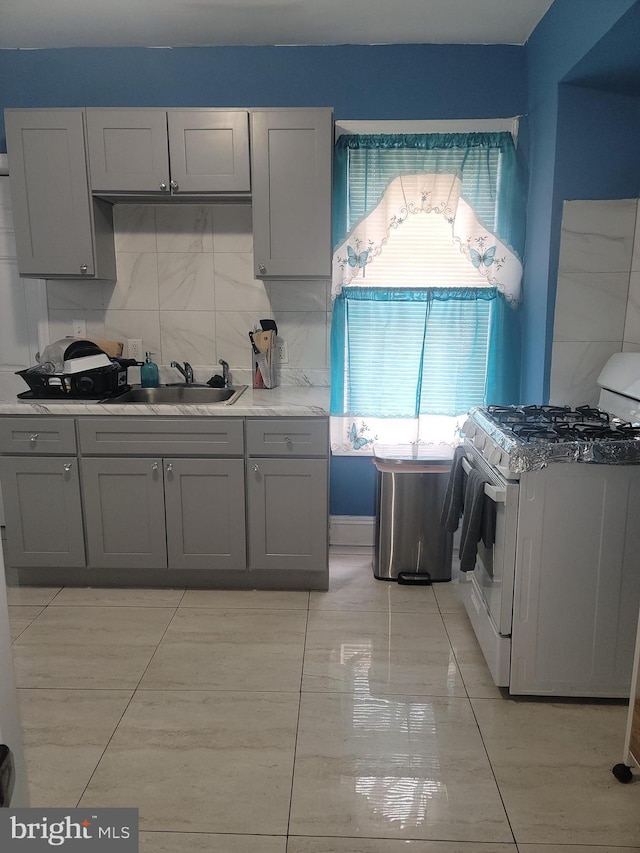 kitchen with light countertops, decorative backsplash, gray cabinetry, a sink, and white gas range oven