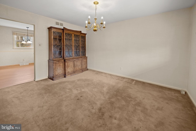 unfurnished dining area featuring a chandelier, carpet flooring, visible vents, and baseboards