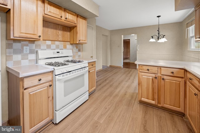 kitchen featuring white range with gas cooktop, light countertops, backsplash, light wood finished floors, and pendant lighting