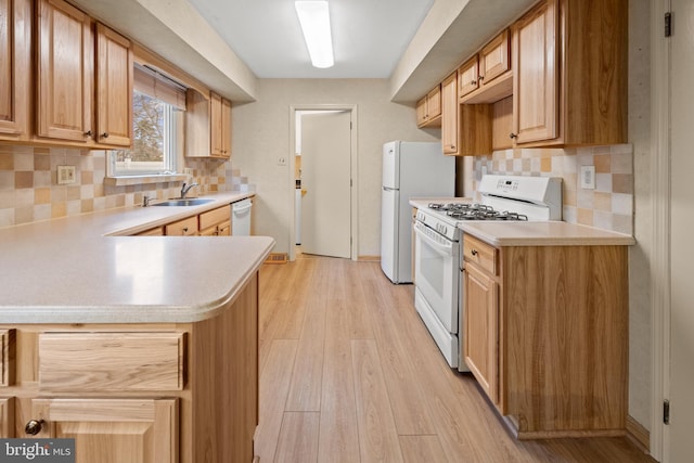 kitchen with light countertops, white appliances, a sink, and light wood-style flooring