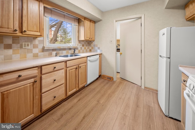 kitchen featuring light wood-style flooring, white appliances, a sink, light countertops, and decorative backsplash