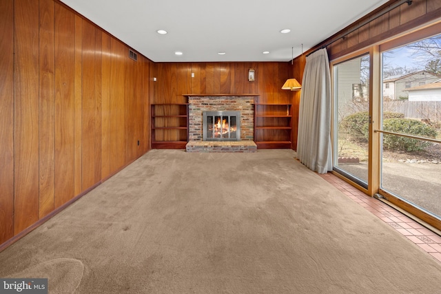 unfurnished living room with recessed lighting, wood walls, a fireplace, visible vents, and carpet