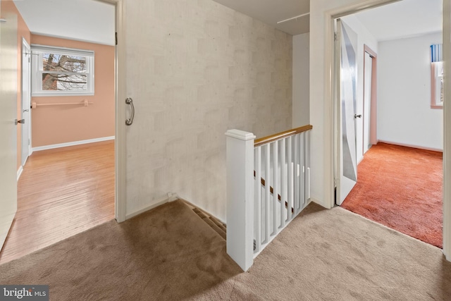 hallway featuring baseboards, carpet flooring, and an upstairs landing