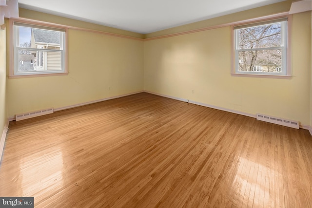 spare room featuring light wood-style flooring, baseboard heating, visible vents, and a healthy amount of sunlight