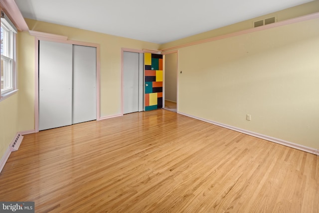 unfurnished bedroom featuring baseboards, wood finished floors, visible vents, and multiple closets