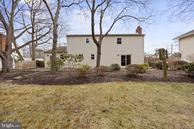 back of house featuring a chimney and a lawn