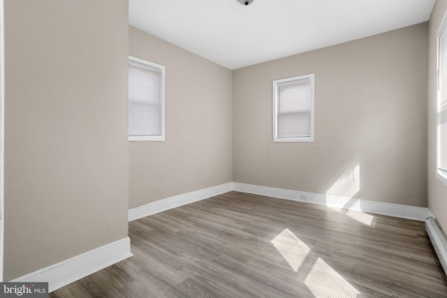 empty room featuring a baseboard heating unit, baseboards, and wood finished floors