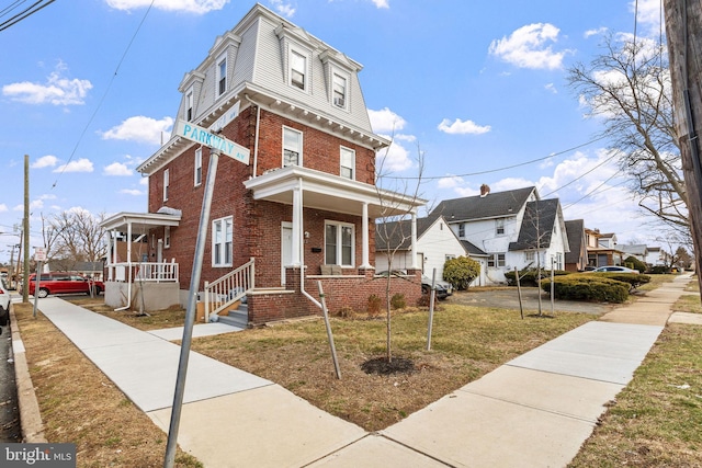 second empire-style home with brick siding, covered porch, mansard roof, and a front yard